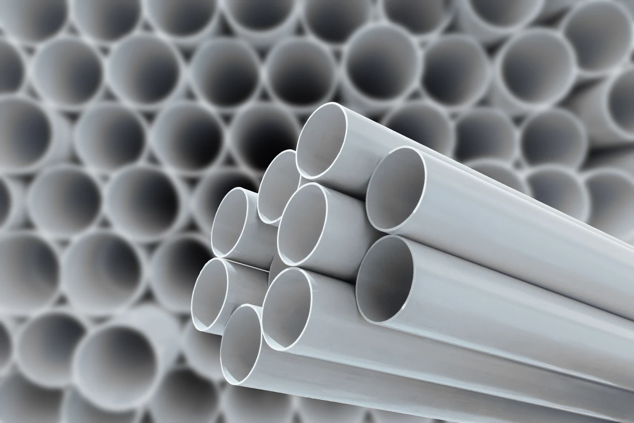 Entrepôt industriel avec stockage de tubes PVC blancs empilés en fagots au premier plan et rangées organisées en arrière-plan