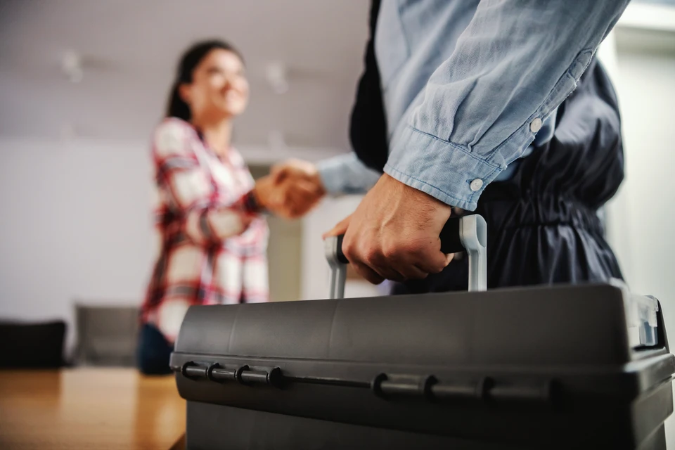 Photographie d'un artisan professionnel en tenue de travail (bleu marine ou logo) discutant face à face avec un client dans un environnement intérieur domestique (salon, cuisine ou autre pièce). L'interaction doit montrer une écoute active : l'artisan face au client, peut-être prenant des notes ou pointant un élément à améliorer, dans une ambiance calme et professionnelle. L'image doit transmettre la confiance, la communication claire et la prise en compte des attentes du client.