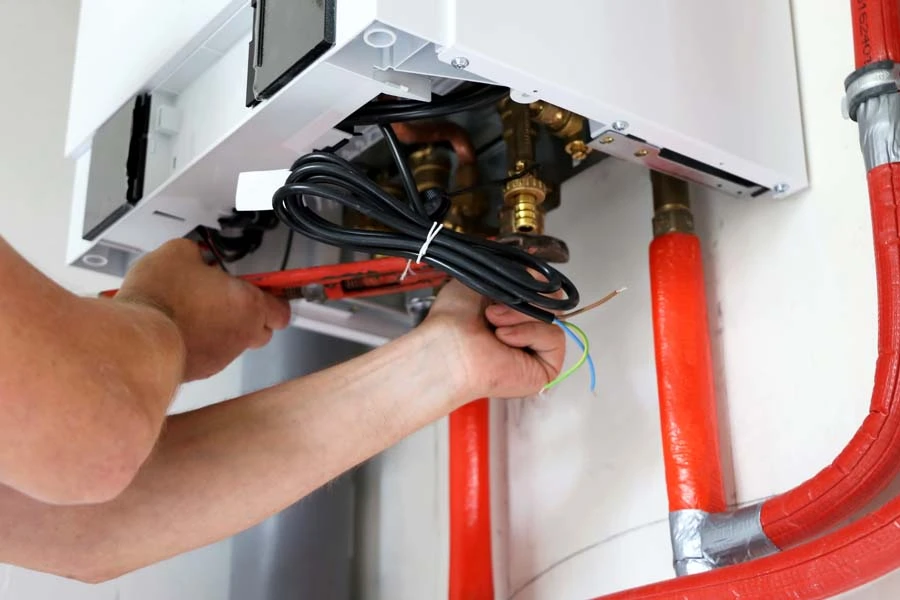 Plombier professionnel travaillant sur une installation de chauffage en intérieur, manipulant des outils sur un système complexe de tuyauterie cuivre et raccords